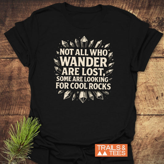 Black T-shirt with NOT ALL WHO WANDER ARE LOST, SOME ARE LOOKING FOR COOL ROCKS slogan surrounded by crystals, labeled Trails & Tees.