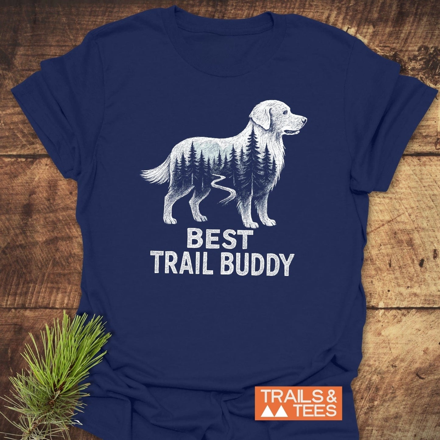 Best Trail Buddy Golden Retriever T-Shirt featuring a retriever line-drawing with pine trees and trail, “BEST TRAIL BUDDY” text, and “TRAILS & TEES” logo on navy fabric.