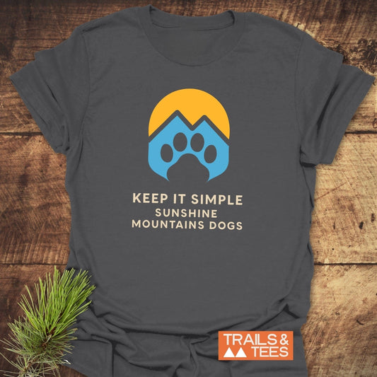 Sun Mountains Dogs T-Shirt on rustic wood, featuring a yellow sun over blue peaks and paw, with slogan. Soft, durable, pre-shrunk cotton for outdoor lovers.