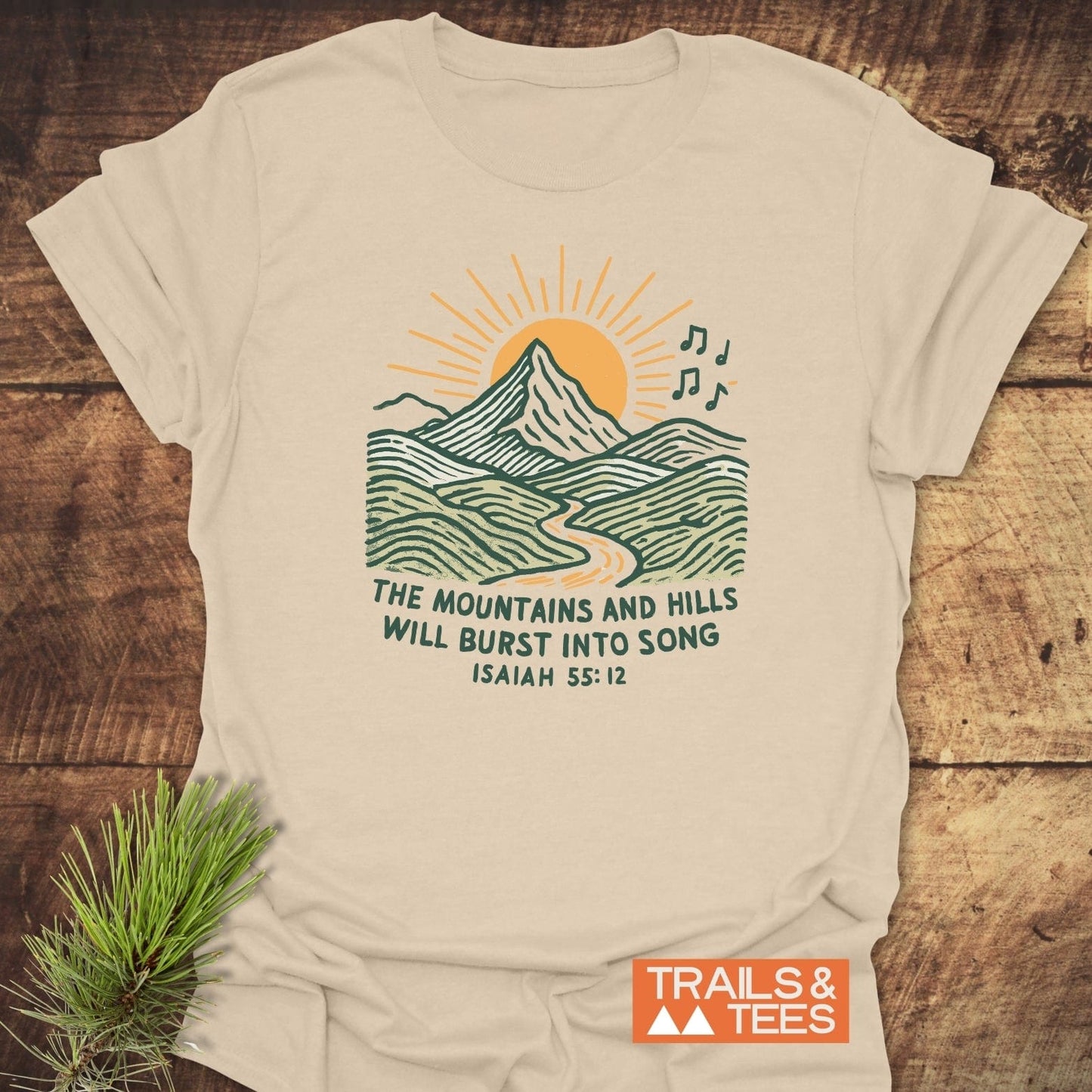 Mountains And Hills T-Shirt with a mountain scene and Isaiah 55:12 text, showcasing nature-inspired design on light-beige cotton for outdoor enthusiasts.