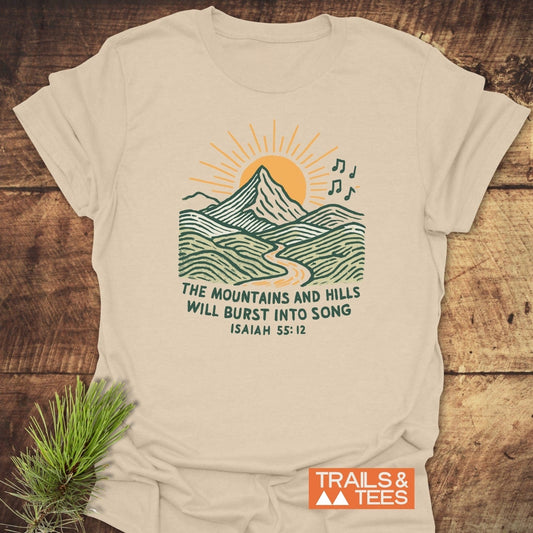 Mountains And Hills T-Shirt with a mountain scene and Isaiah 55:12 text, showcasing nature-inspired design on light-beige cotton for outdoor enthusiasts.