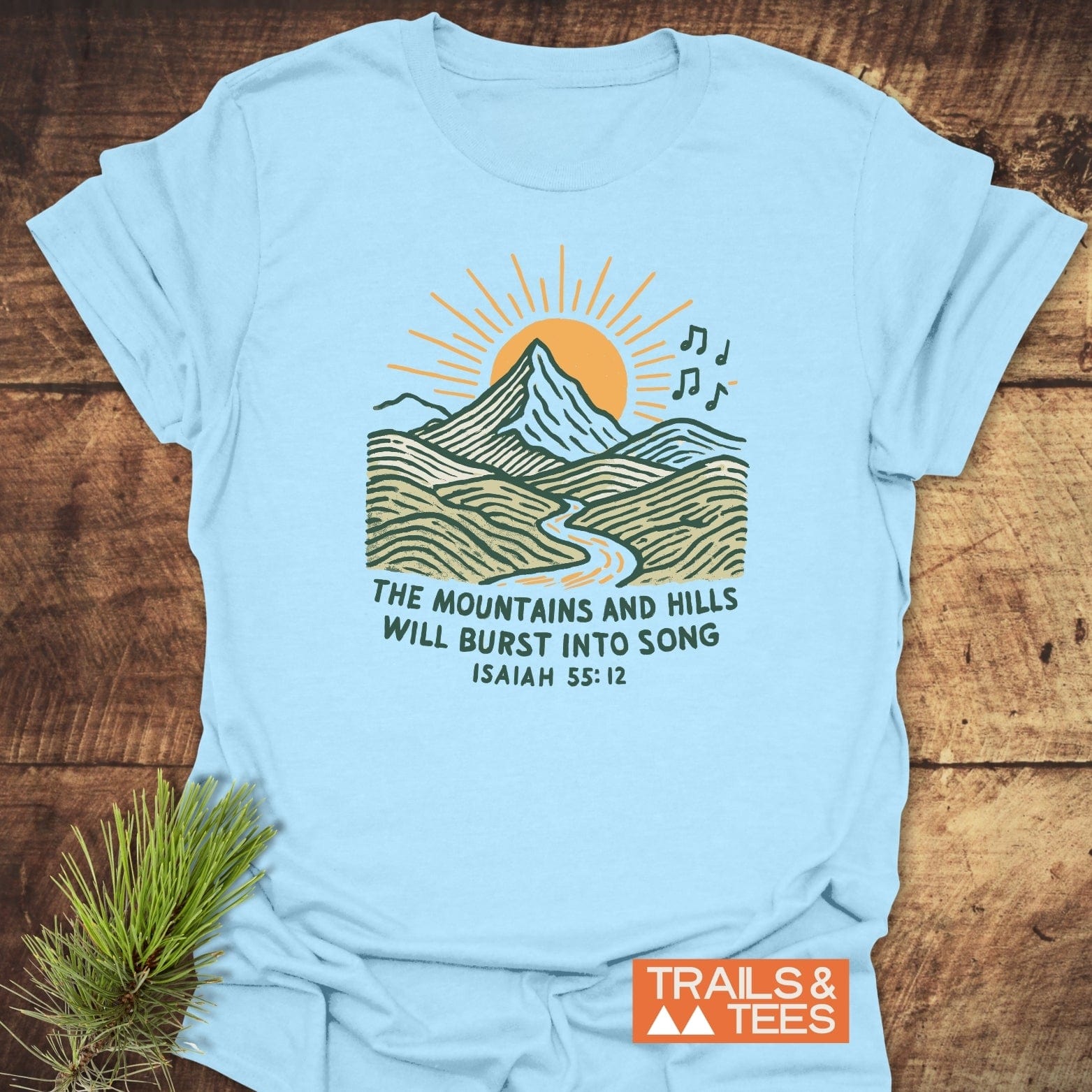 Mountains And Hills T-Shirt with a sunrise mountain illustration and Isaiah 55:12 verse, laid flat. Features durable print, soft cotton, and taped shoulders for comfort.