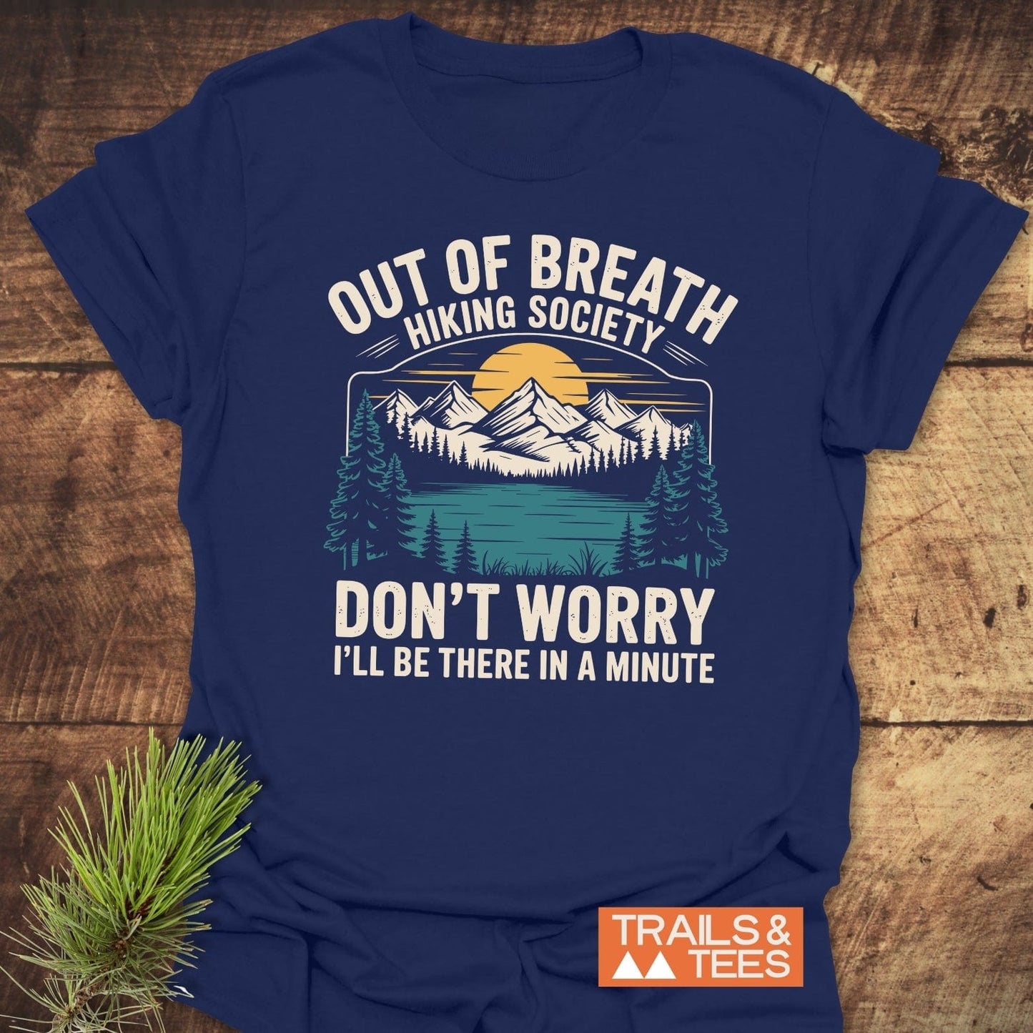 Navy-blue t-shirt with Out Of Breath Hiking Society graphic of sunset, mountains, pine forest, and lake. Features durable print, soft cotton, pre-shrunk fit.