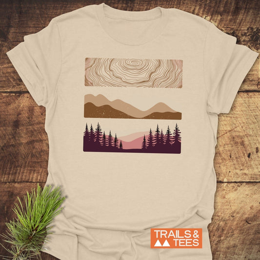 Minimalist Mountains Graphic T-Shirt with topographic, mountain, and forest designs on cream fabric, showcasing outdoor spirit. Includes TRAILS & TEES logo.