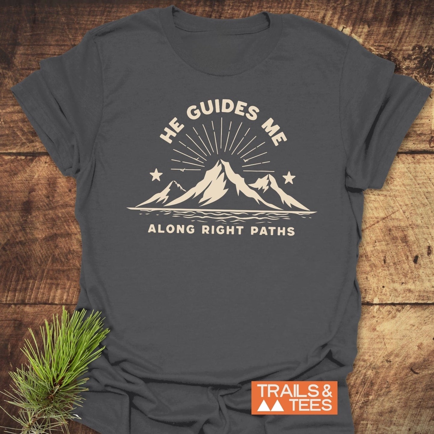 He Guides Me T-Shirt with mountain and sunbeam graphic, crafted from soft cotton. Features durable prints, pre-shrunk fit, and is styled with a pine sprig.