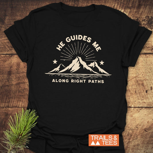 He Guides Me T-Shirt featuring a mountain graphic with sun-rays, crafted from soft cotton. Includes durable prints and a small Trails & Tees logo.