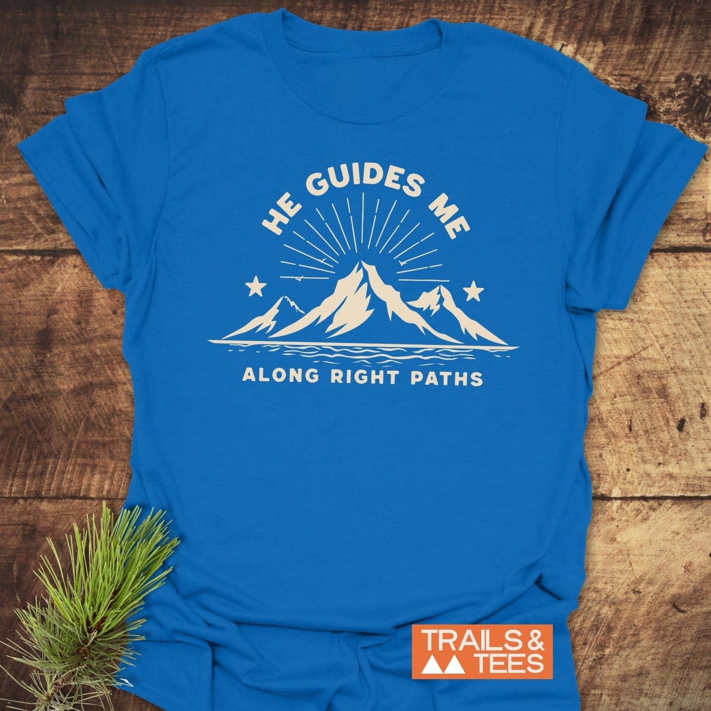 He Guides Me T-Shirt with mountain design, sunburst, and stars; features durable prints, pre-shrunk fit, crafted for comfort, with 'Trails & Tees' logo.