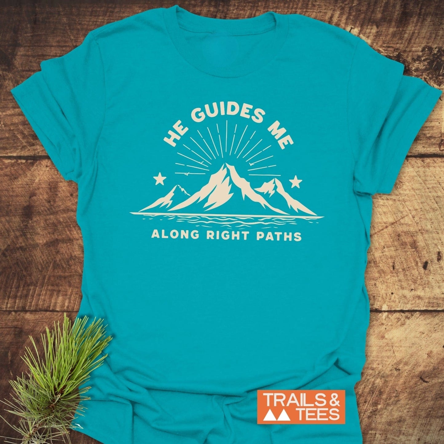 He Guides Me T-Shirt with mountain graphic and text, made from soft ring-spun cotton, featuring durable DTF prints and a Trails & Tees logo.