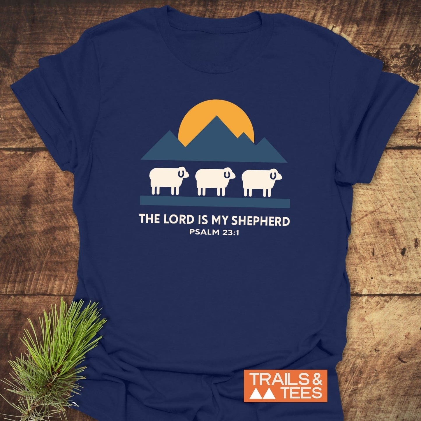Navy-blue tee featuring golden sun, blue mountains, and sheep graphic with THE LORD IS MY SHEPHERD text, epitomizing adventure and comfort.