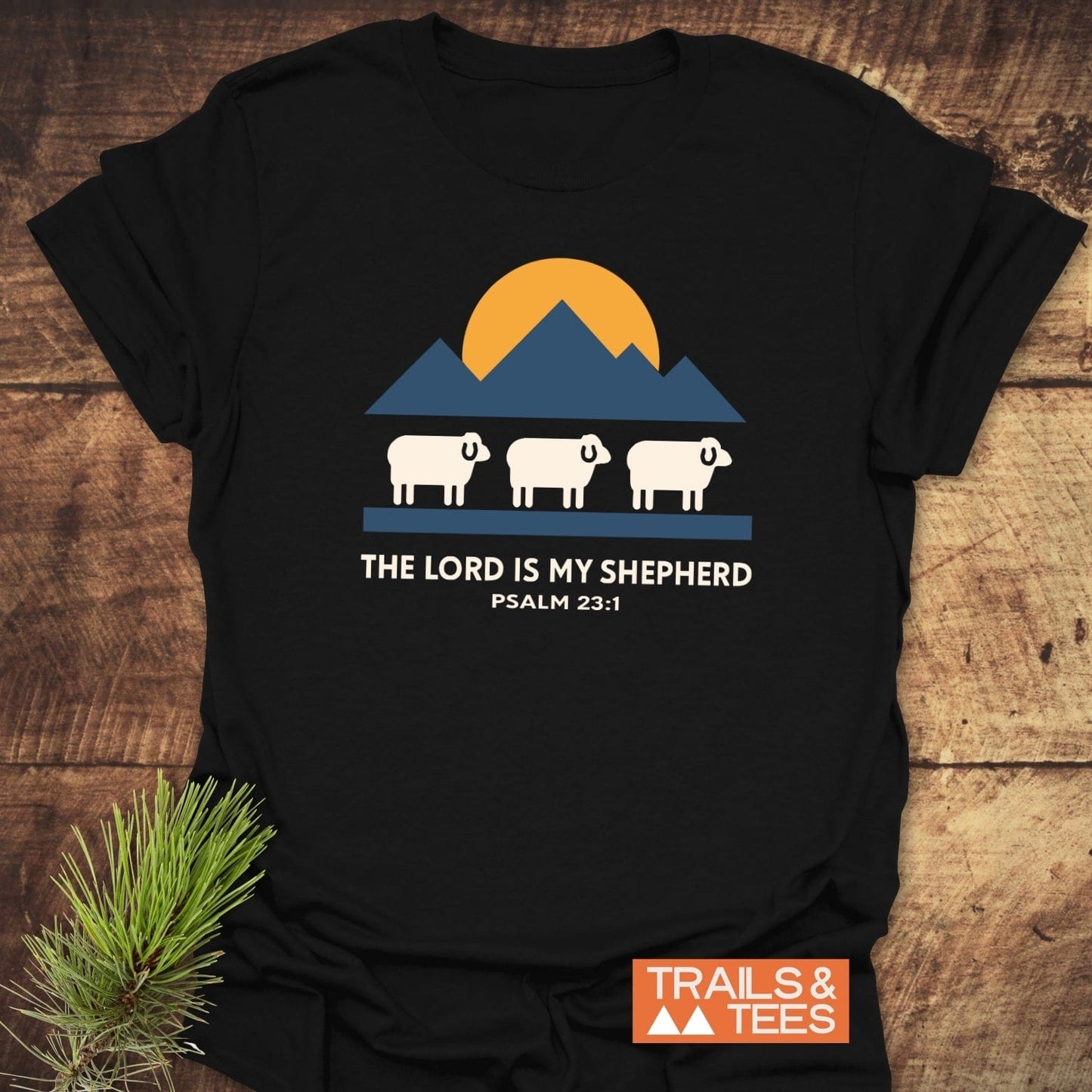 The Lord Is My Shepherd T-Shirt features a sun, mountains, and sheep graphic, with Psalm 23:1 text, crafted from soft cotton for outdoor comfort.