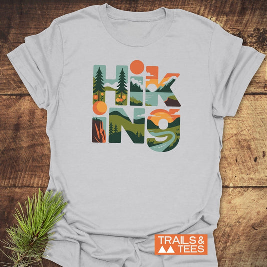 Hiking Typographic T-Shirt with outdoor scene letters, laid on wood with pine branch; features durable prints, soft cotton, and eco-friendly on-demand production.
