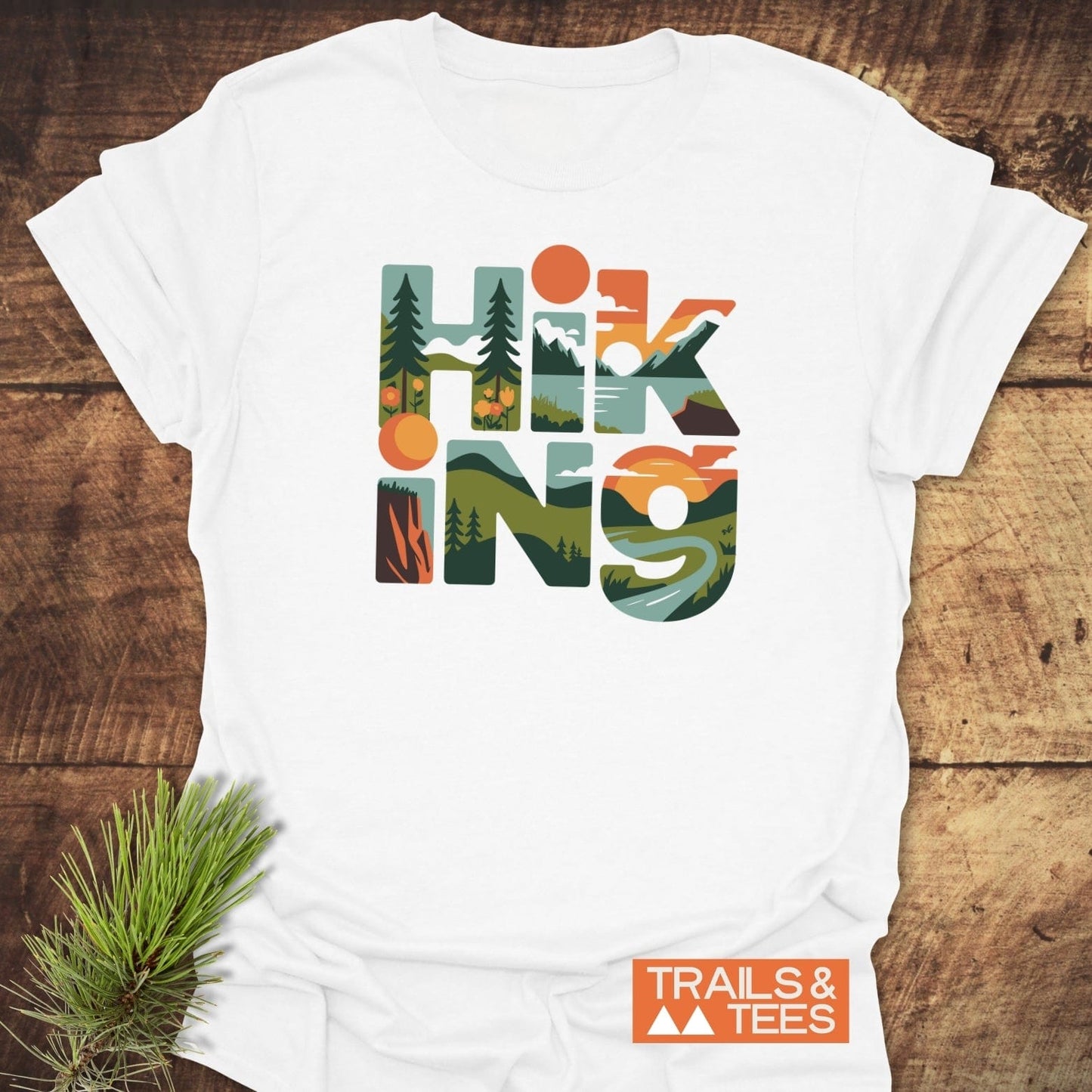 Hiking Typographic T-Shirt featuring nature-filled letters on white cotton, styled with a pine sprig, and Trails & Tees logo. Ideal for outdoor enthusiasts.