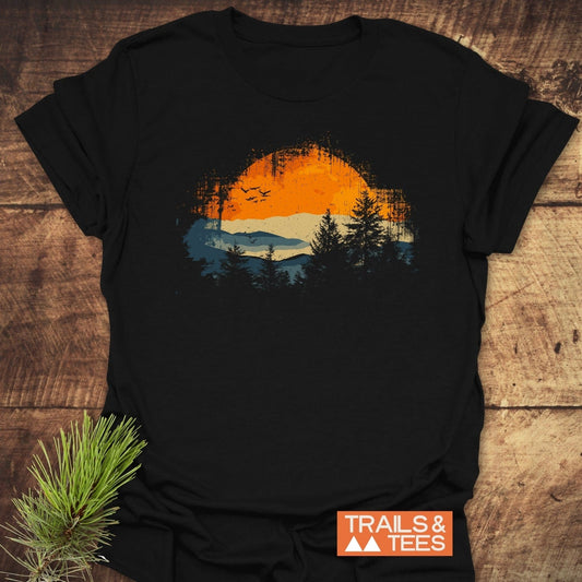 Great Smoky Mountains T-Shirt with a circular landscape graphic, featuring silhouetted pine trees and birds, laid on wood with a pine sprig.