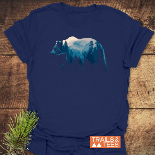Grizzly Silhouette T-Shirt featuring a bear with pine trees and mountain graphic, laid on wood. Includes TRAILS & TEES logo, highlighting adventure-ready design.