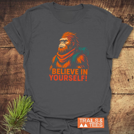 Believe In Yourself Bigfoot T-Shirt on rustic wood, featuring a bold illustration of Bigfoot in a scarf, with durable, adventure-ready design and comfort-focused craftsmanship.