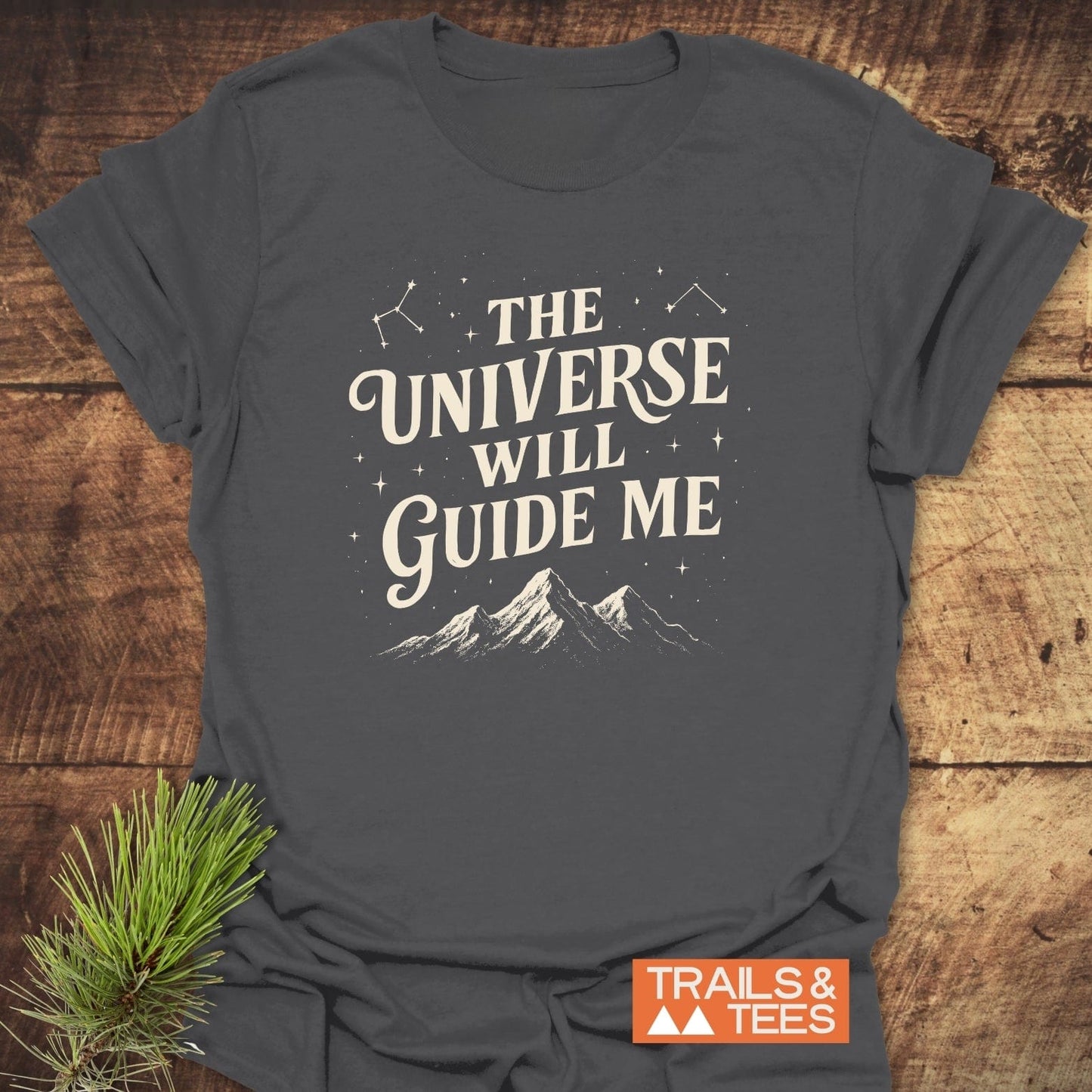 The Universe Guides Me T-Shirt with cream hand-lettered text, stars, constellations, and mountains. Soft ring-spun cotton, durable print, designed for outdoor enthusiasts.