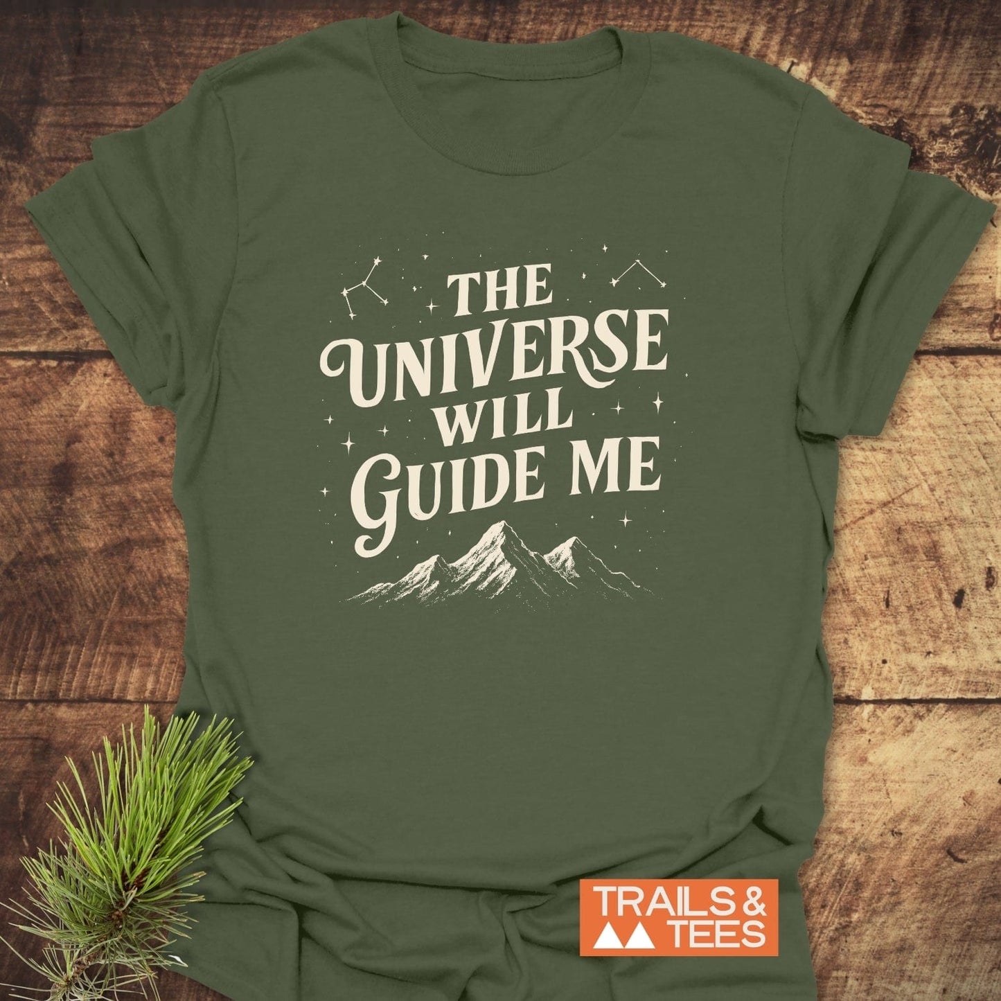 Forest-green The Universe Guides Me T-shirt with cream print: mountain silhouette, stars. Comfortable ring-spun cotton, pre-shrunk, durable print. TRAILS & TEES logo visible.