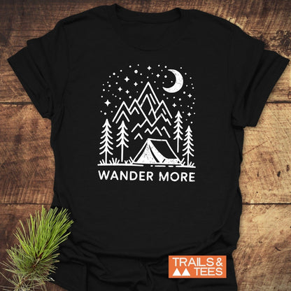 Wander More T-Shirt featuring a camping scene with pine trees, mountains, and stars, printed on soft cotton. Includes TRAILS & TEES logo.