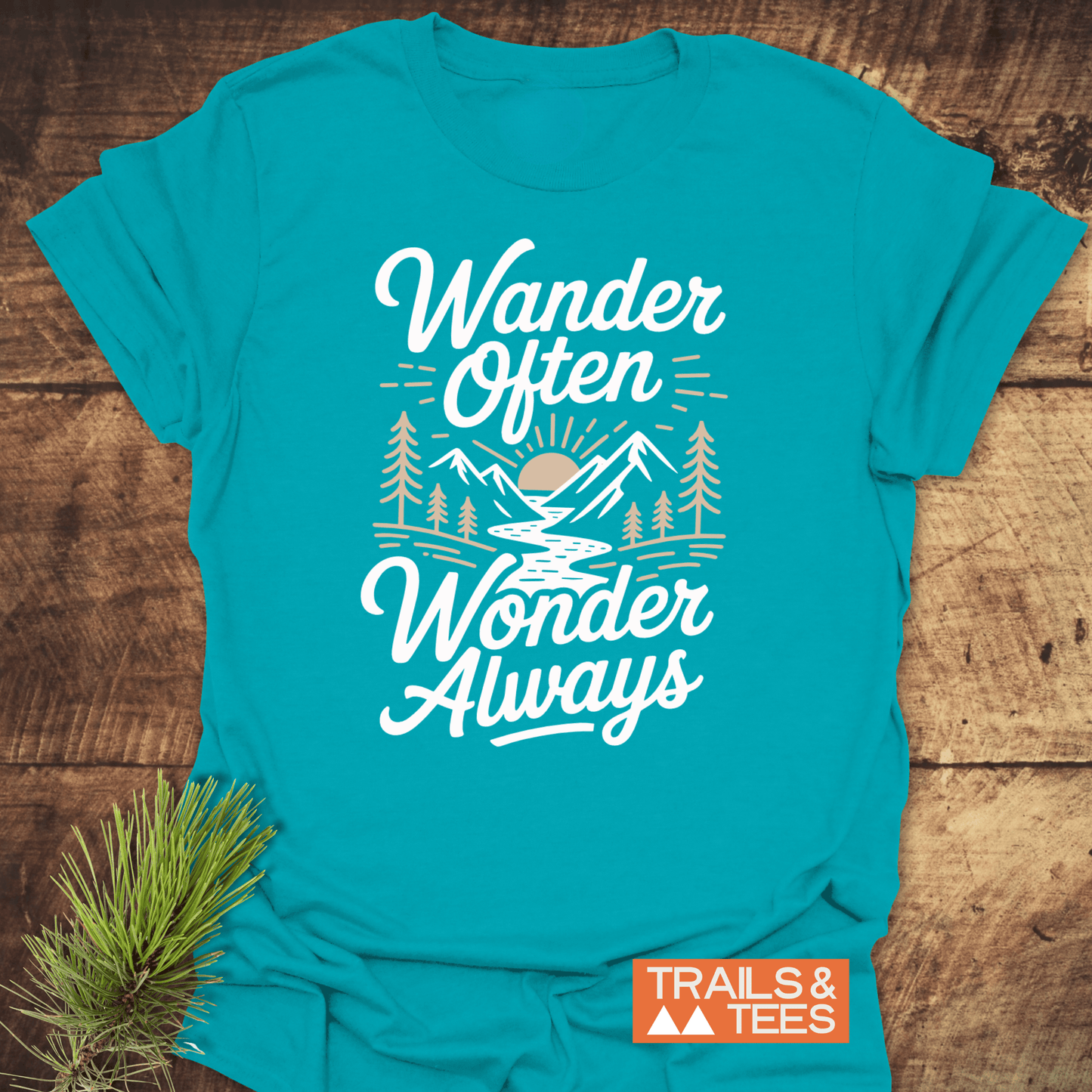 Wander Often T-Shirt with outdoor graphic of river, trees, mountains, and sun. Features slogan, Wander Often Wonder Always, by TRAILS & TEES.