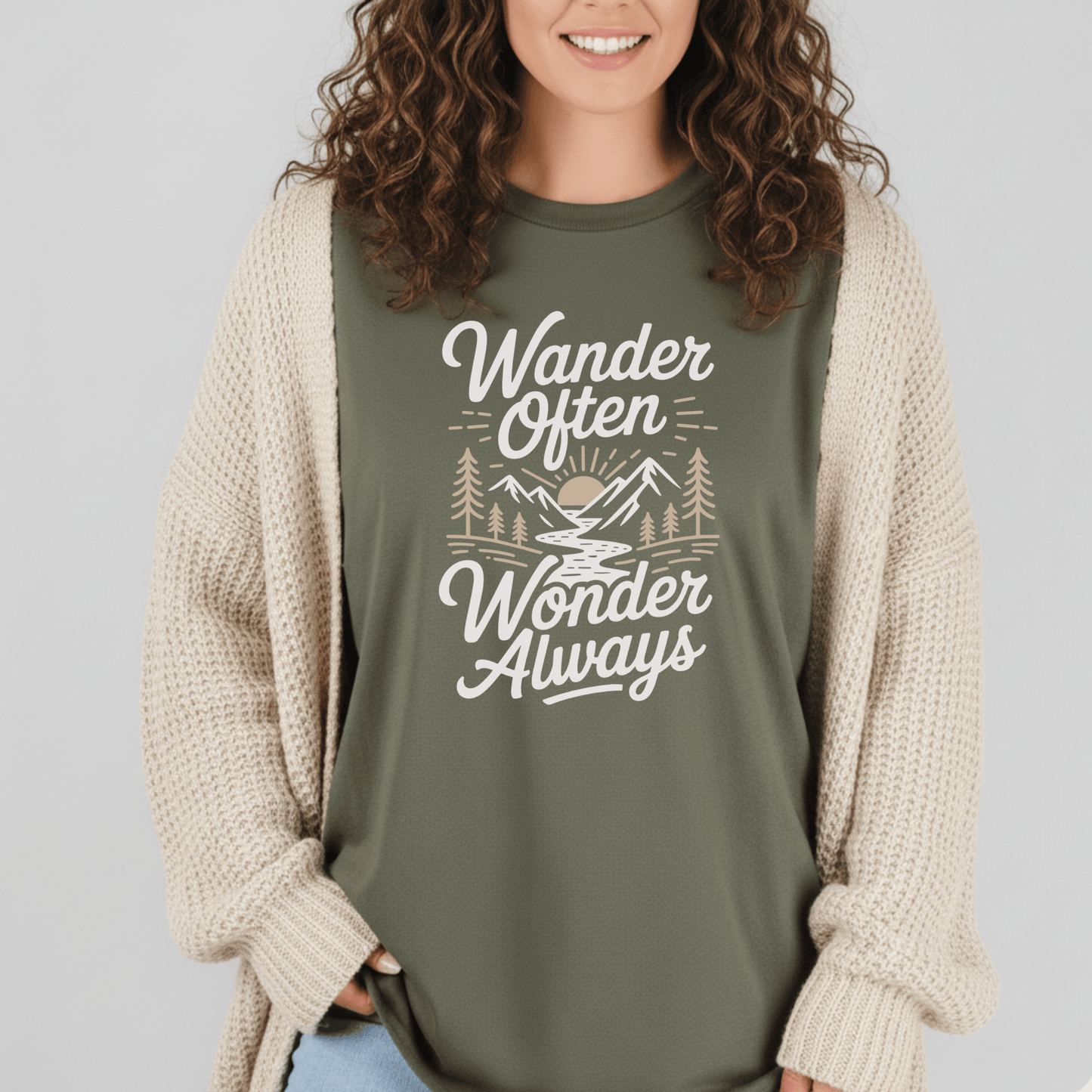Person wearing Wander Often T-Shirt with mountain scene design, layered over a chunky knit cardigan, showcasing casual style and outdoor adventure spirit.