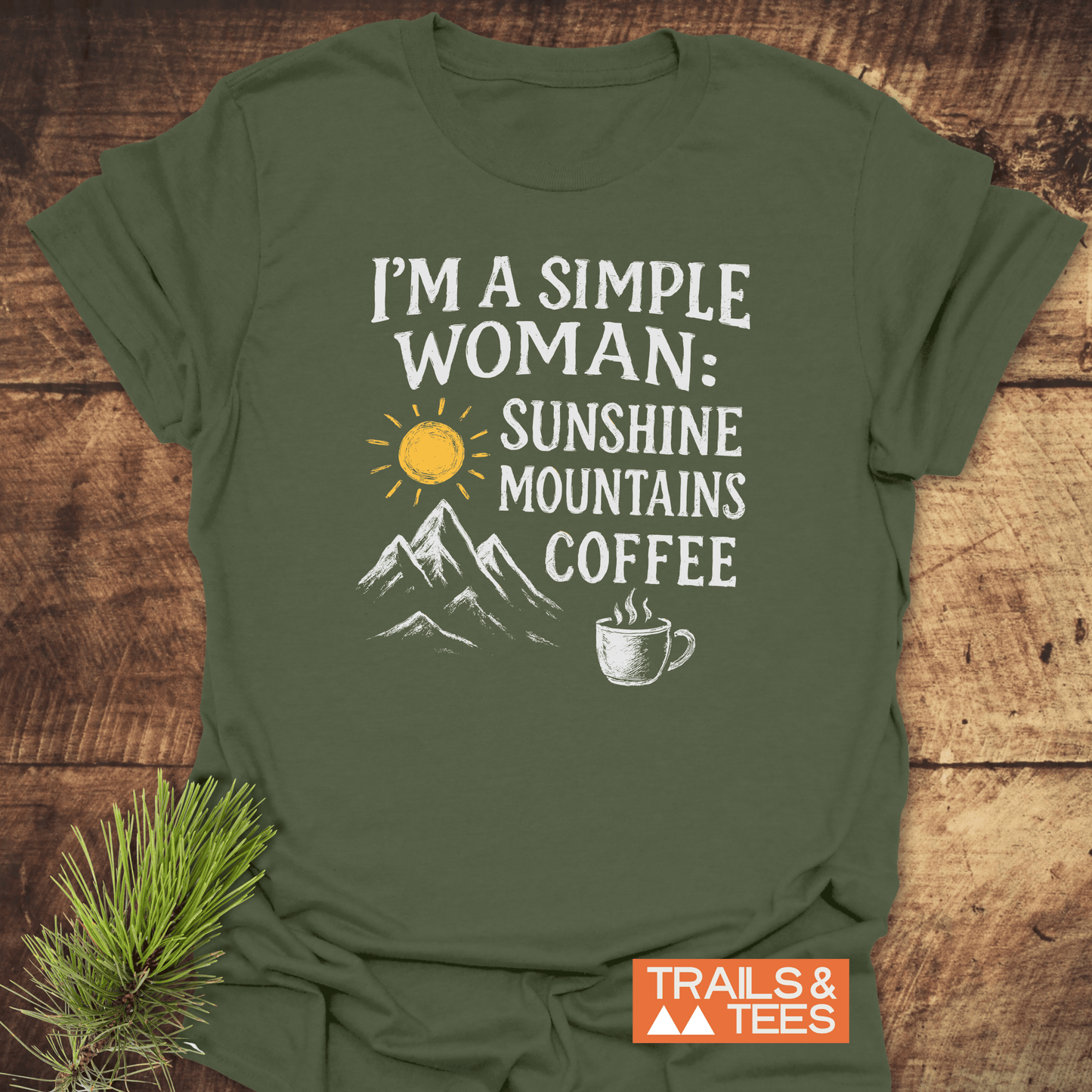 Simple Woman Sunshine T-Shirt with a rustic graphic of a sun, mountains, and coffee mug, laid flat on wood; showcases outdoor adventure spirit.