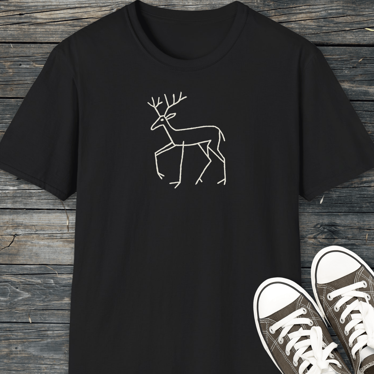 Deer Tribal T-Shirt in black with a white deer line-drawing, displayed on wooden planks, paired with canvas sneakers. Crafted from soft, durable cotton for outdoor adventures.