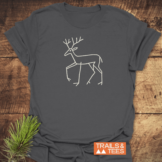Deer Tribal T-Shirt featuring a line drawing of a deer with antlers, showcasing petroglyph-style design, on a charcoal-gray fabric. Includes TRAILS & TEES logo.