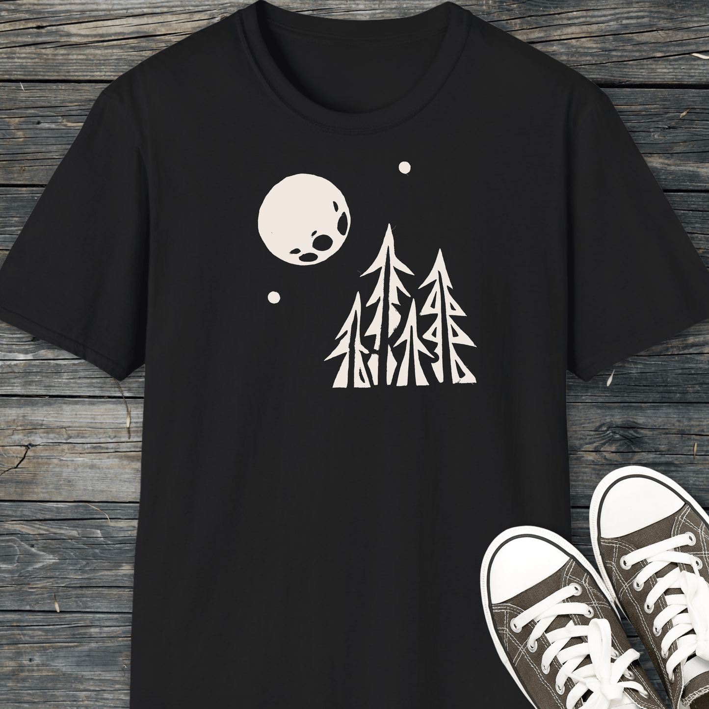 Black Pine Trees and Full Moon T-shirt with white graphic, laid flat. Accompanied by dark canvas sneakers, highlighting the shirt's outdoor-inspired design and comfort.