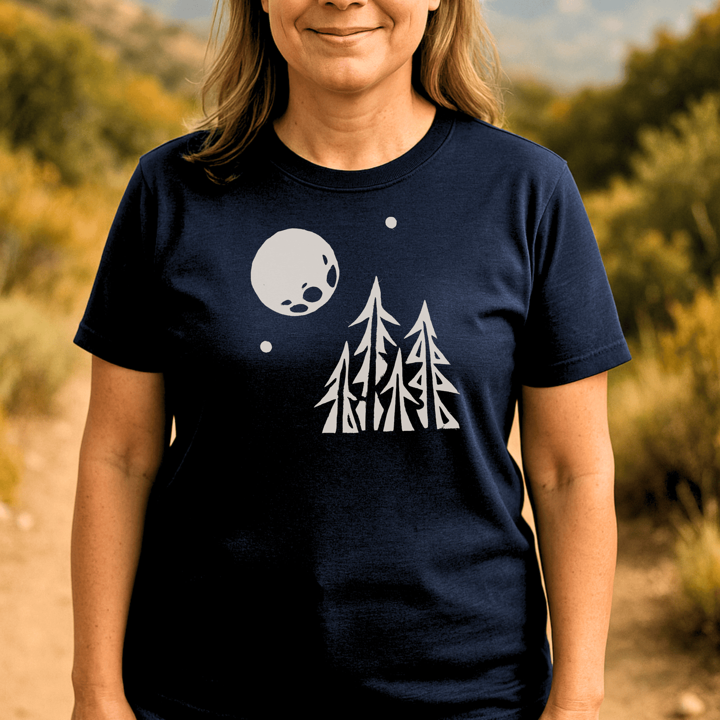 Pine Trees and Full Moon T-Shirt showcasing a stylized graphic of pine trees and a moon, worn in a desert landscape, highlighting its casual outdoor appeal.