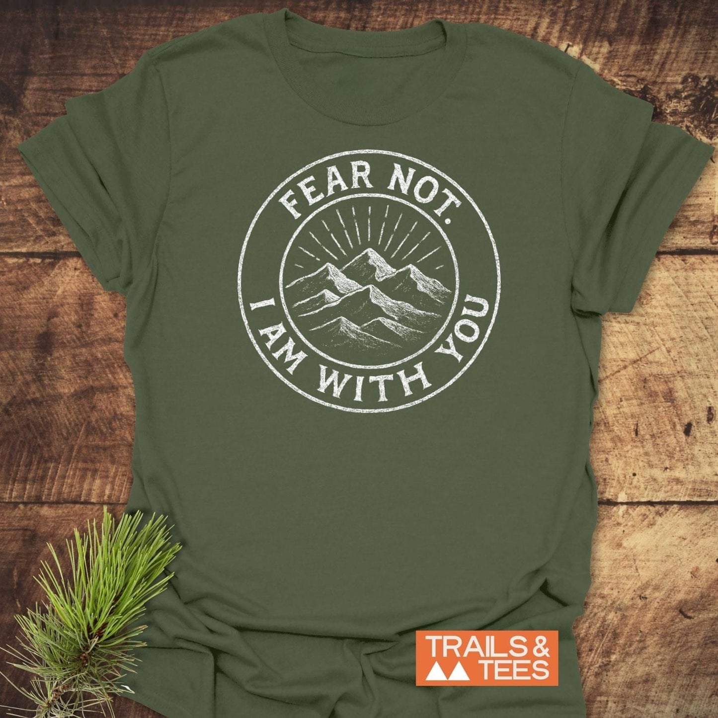 Fear Not Mountain T-Shirt featuring a mountain graphic and “FEAR NOT, I AM WITH YOU” on a forest-green tee, with an orange TRAILS & TEES logo tag.