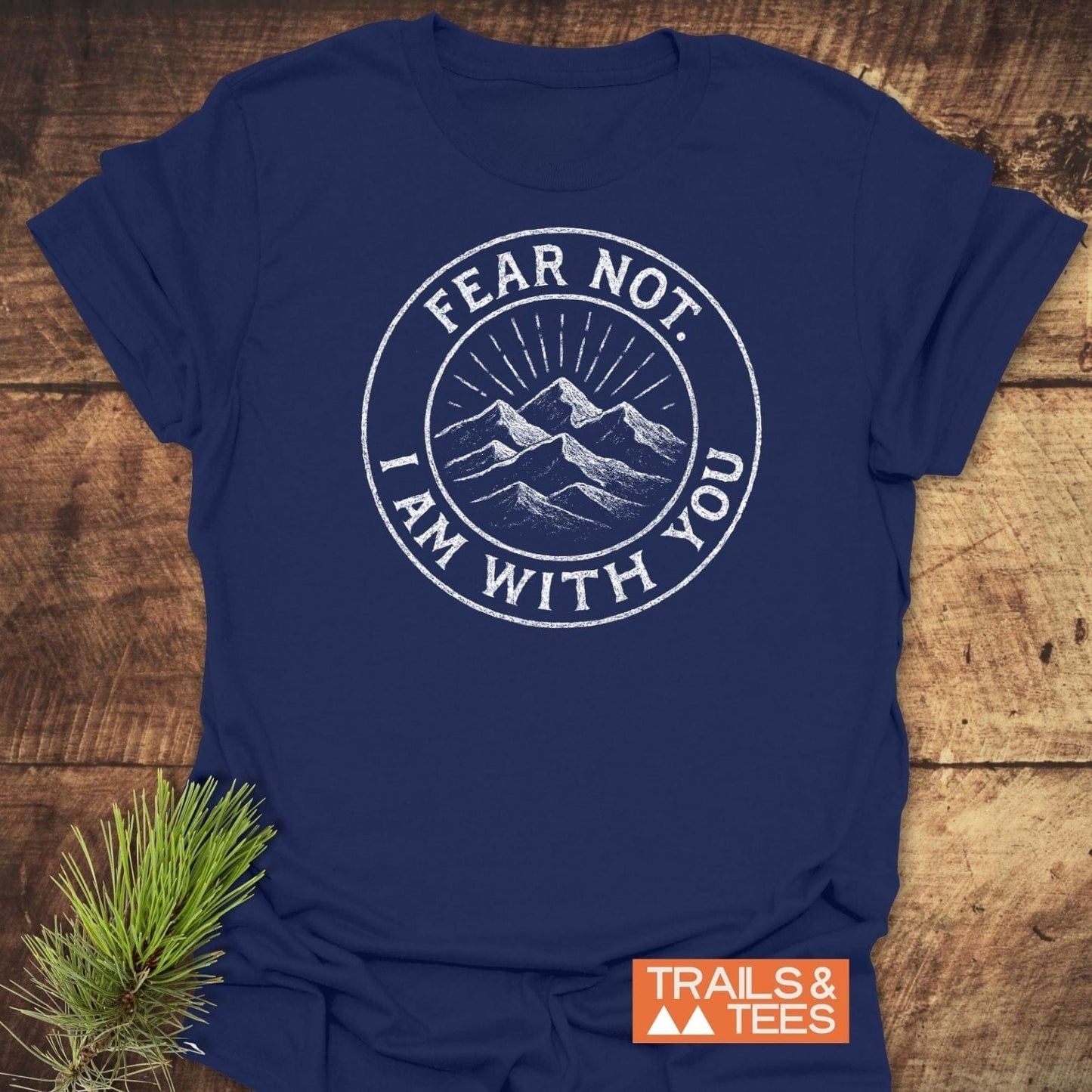 Fear Not Mountain T-Shirt with a white mountain graphic and sunrays, emphasizing outdoor adventure. Laid flat with a pine sprig beside it.