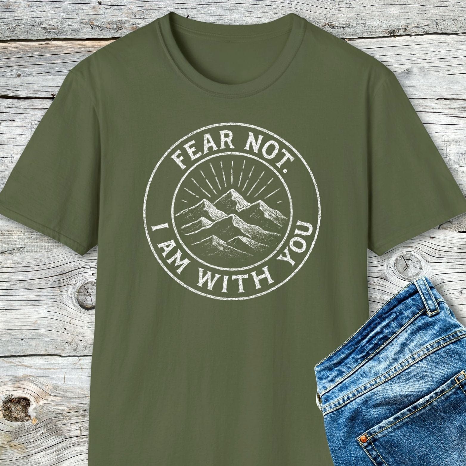 Fear Not Mountain T-Shirt with white mountain graphic and motivational text, paired with blue denim jeans on a wooden background, showcasing outdoor-inspired style and comfort.