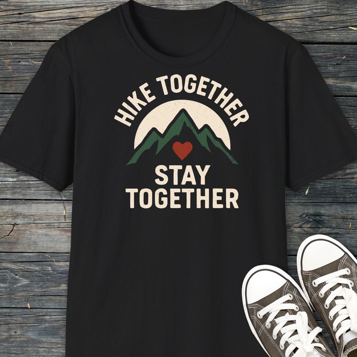 Hike Together Couple T-Shirt featuring green mountains and a sun graphic, laid on wood, with canvas sneakers nearby. Soft, ring-spun cotton for outdoor adventures.