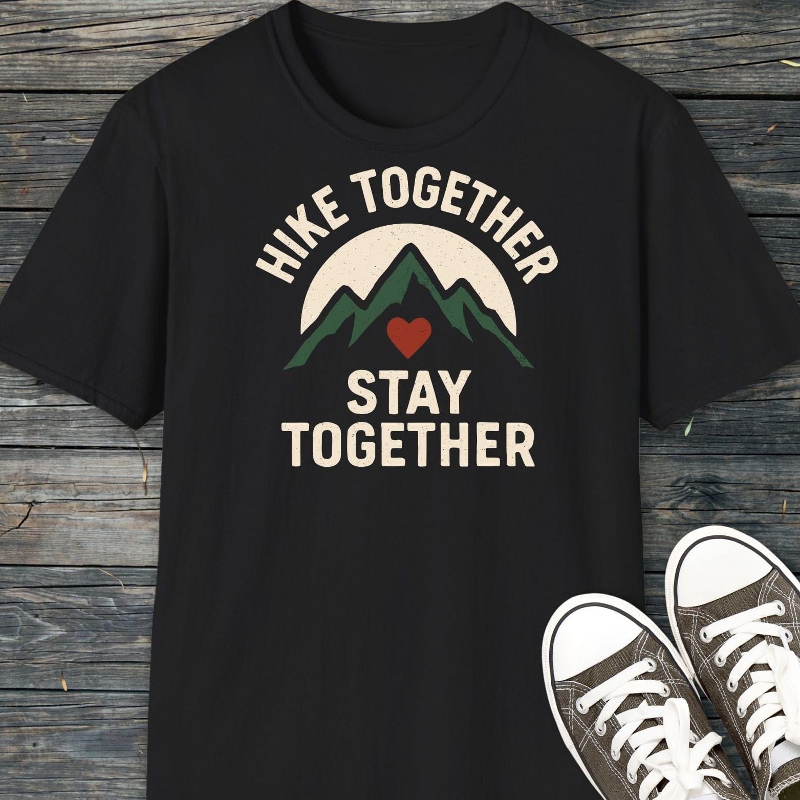Hike Together Couple T-Shirt featuring green mountains and a sun graphic, laid on wood, with canvas sneakers nearby. Soft, ring-spun cotton for outdoor adventures.