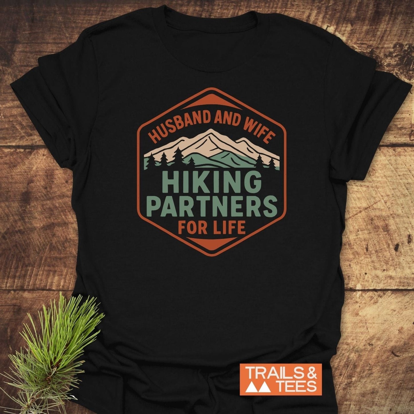 Hiking Partners For Life T-Shirt featuring a mountain and pine tree graphic, crafted from soft ring-spun cotton, displayed flat with pine sprig, brand logo visible.
