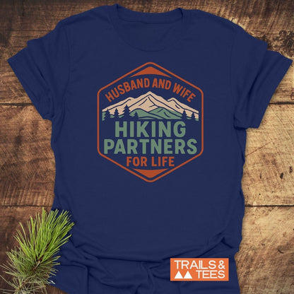 Navy-blue Hiking Partners For Life T-shirt featuring a mountain badge graphic, laid on wood, highlighting durable, soft cotton for outdoor enthusiasts.