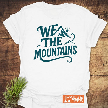 We The Mountains T-Shirt featuring a teal mountain design on white cotton, showcasing trail-ready comfort and durability, with a pine sprig accent.