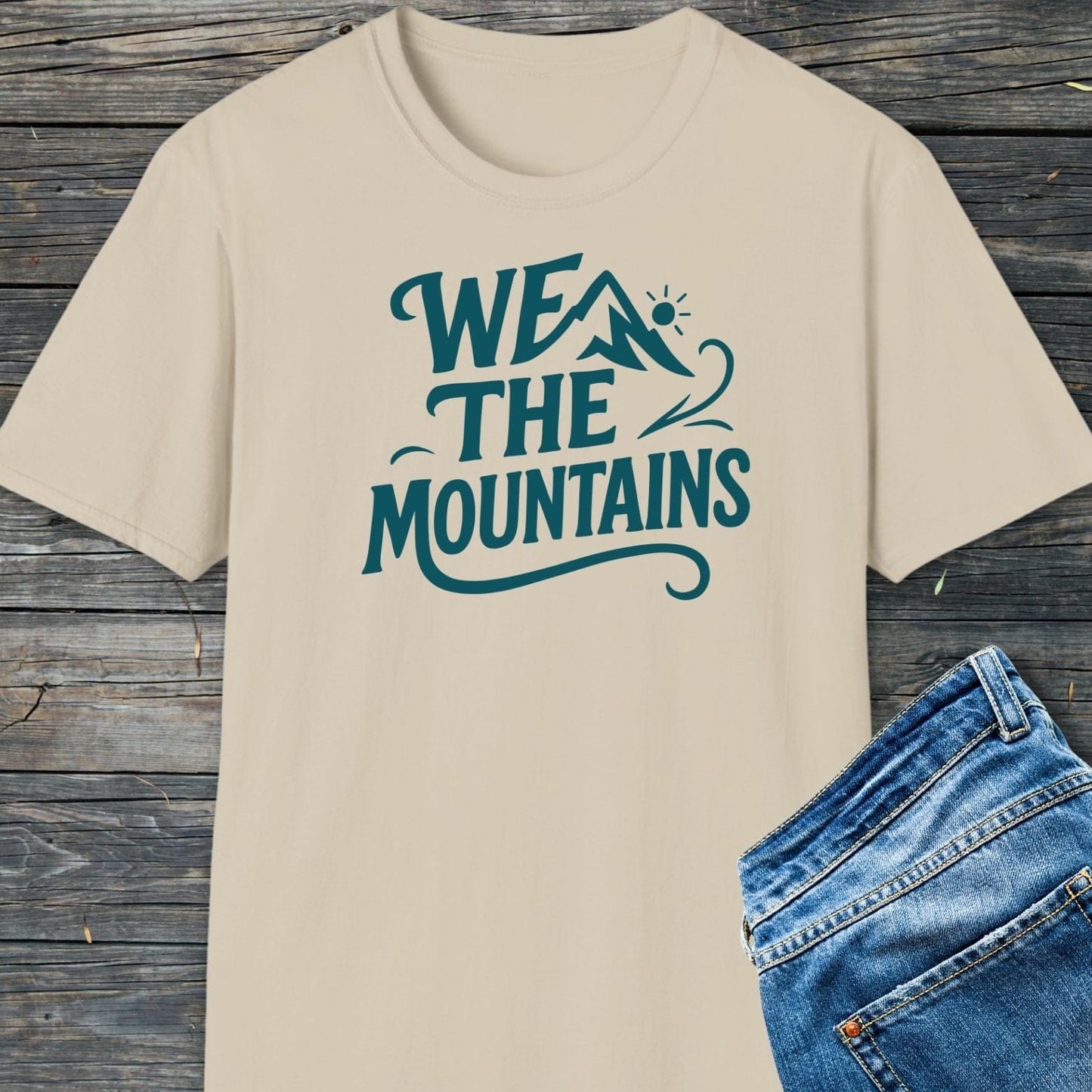 We The Mountains T-Shirt featuring teal mountain graphic, laid with jeans; made from soft, ring-spun cotton for comfort, perfect for outdoor enthusiasts.