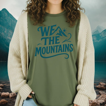 Woman wearing We The Mountains T-shirt under a cardigan, featuring a mountain graphic and slogan, embodying adventure-ready, lightweight comfort for outdoor enthusiasts.