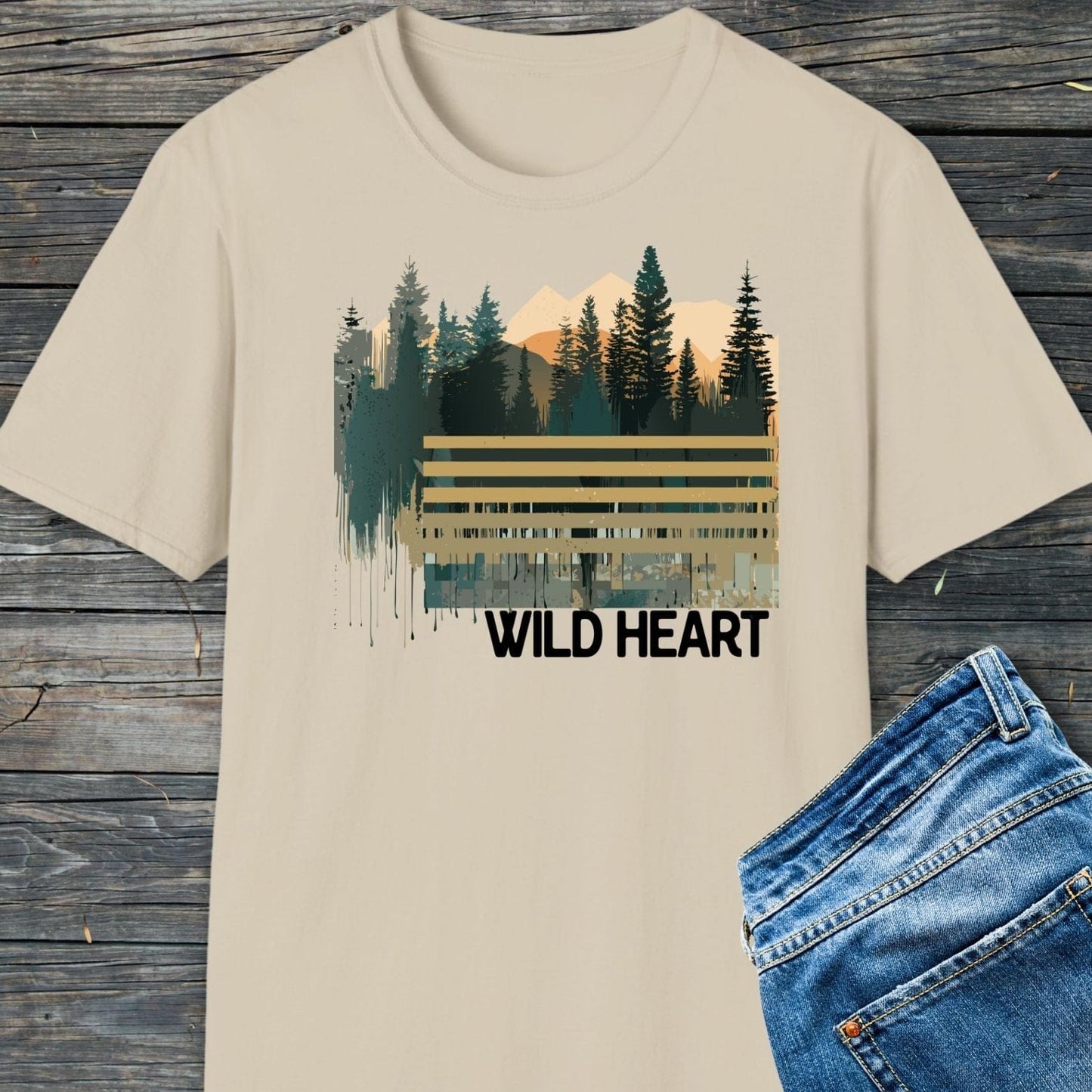Wild Heart Graphic T-Shirt featuring a forest and mountain print, laid with blue jeans. Soft, durable, and pre-shrunk for outdoor enthusiasts.