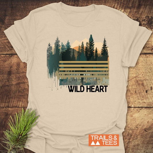 Wild Heart Graphic T-Shirt featuring a mountain-and-forest design, displayed on wood with pine sprig. Made from soft, durable cotton for outdoor enthusiasts.