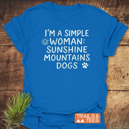 Sunshine Mountains Dogs T-Shirt with sun and paw icons, laid on wood. Features soft cotton, pre-shrunk fit, and durable print. Includes TRAILS & TEES logo.