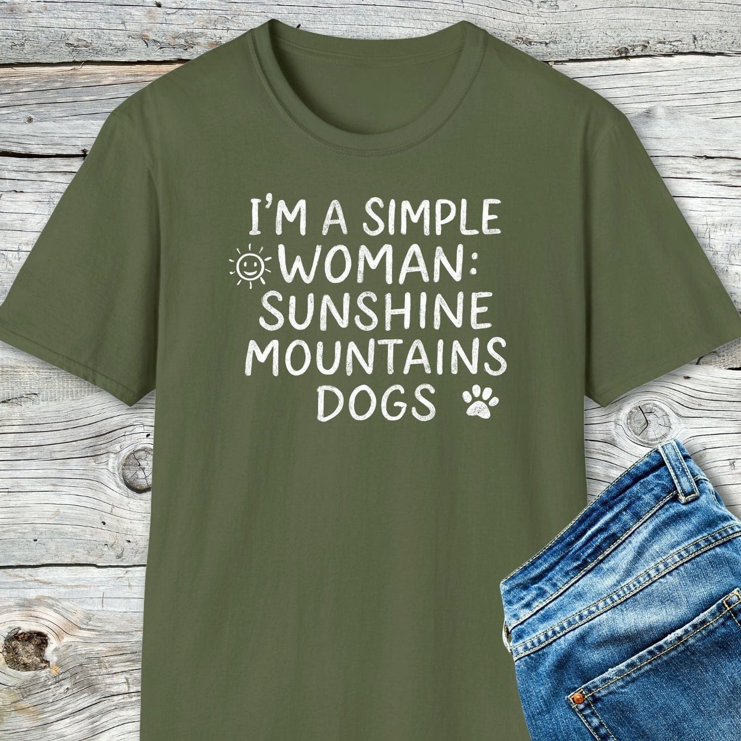 Sunshine Mountains Dogs T-Shirt with slogan and icons, laid flat with blue jeans. Soft ring-spun cotton, pre-shrunk, durable prints for outdoor enthusiasts.