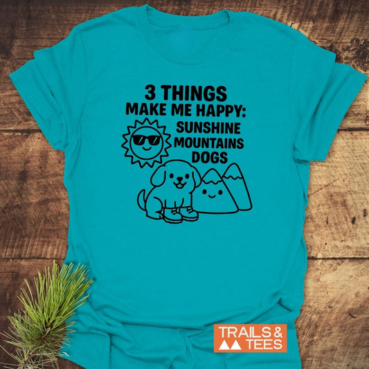 Sunshine Mountains Dogs T-Shirt: Teal shirt with happy icons—sun, mountains, puppy—celebrating outdoor joy. Features Trails & Tees logo and pine sprig accent.