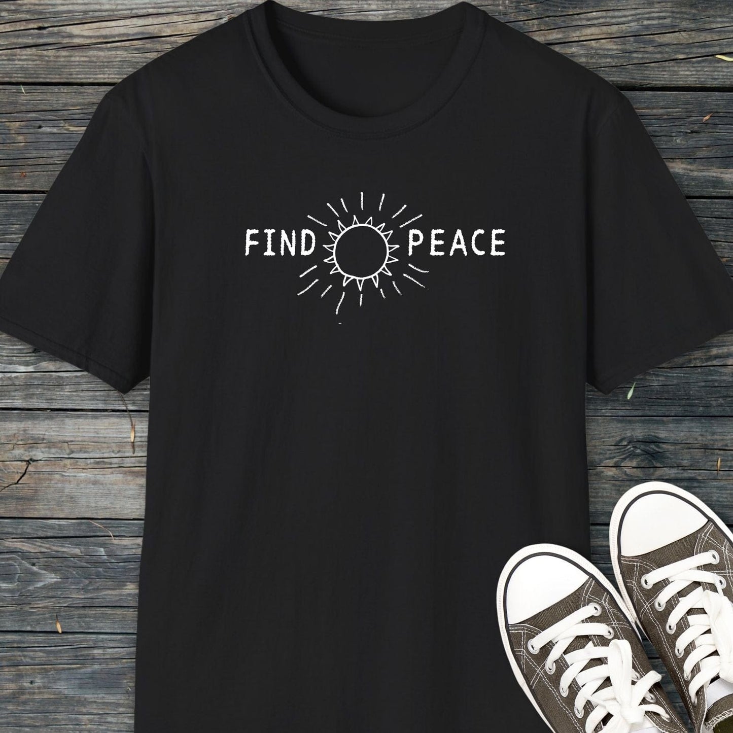 Find Peace T-Shirt with white FIND PEACE graphic and sun outline on chest, laid on wood, paired with casual canvas sneakers.