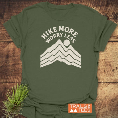 Hike More Worry Less T-Shirt featuring a mountain-and-sun graphic, laid flat with branding tag. Ideal for outdoor enthusiasts, crafted for comfort and durability.