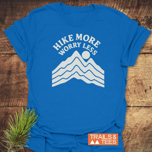 Hike More Worry Less T-Shirt features a mountain-and-sun graphic, emphasizing outdoor adventure. Made from soft, durable cotton with a TRAILS & TEES logo.