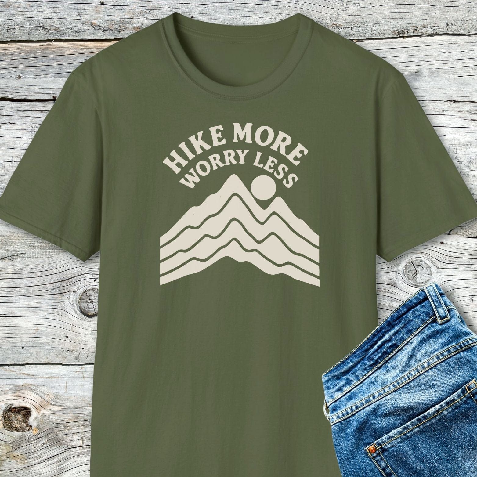 Hike More Worry Less T-Shirt featuring a cream mountain and sun graphic, highlighting its soft ring-spun cotton and durable print on a wooden backdrop.