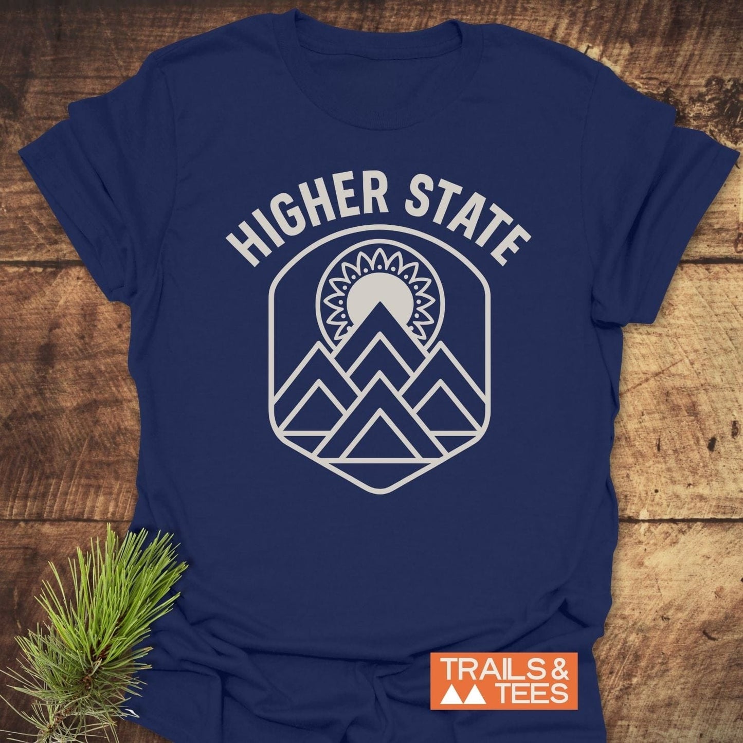 Higher State Mountain Mandala T-Shirt with geometric mountain and sun design, featuring durable prints and taped shoulders. Includes TRAILS & TEES label.