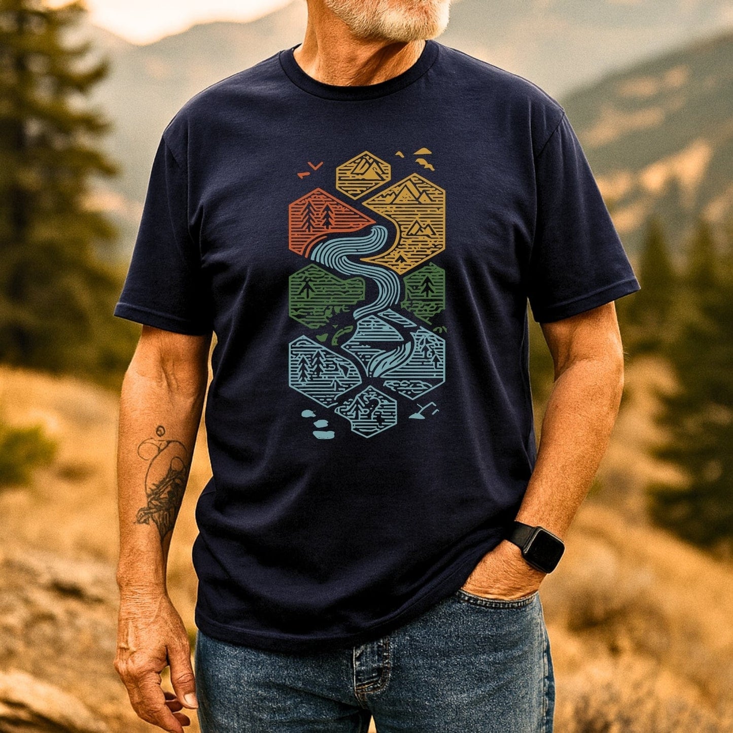 Person wearing Everything Flows T-Shirt with hexagonal landscape design, dark navy color, paired with blue jeans, showcasing outdoor-inspired style and comfort.